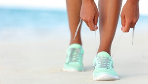 Runner woman tying laces of running shoes preparing for beach jogging. Closeup of hands lacing cross training sneakers trainers for cardio workout. Female athlete living a fit and active life.