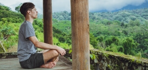 Young fashionable man meditating in the gazebo on the background of the mountains in Bali