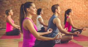 Side view of beautiful sports people sitting in lotus position while doing yoga in modern fitness hall